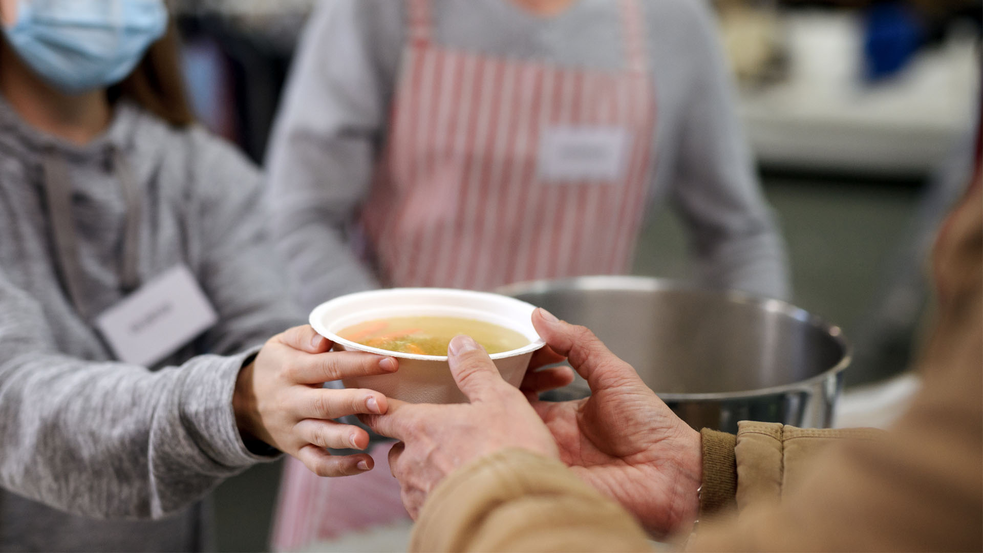 Volunteers serving hot soup for homeless in community charity donation center, coronavirus concept.